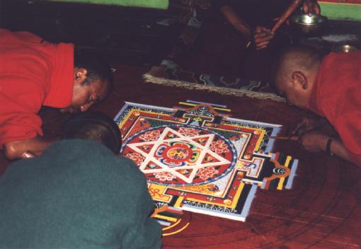 Im Gebetsraum des Klosters arbeiten vier Mönche an einem Mandala aus Farbpulvern.